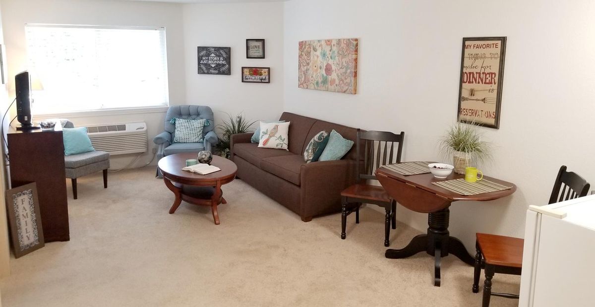 A cozy living room with a brown sofa, wooden coffee table, blue armchair, and wall art decorations.