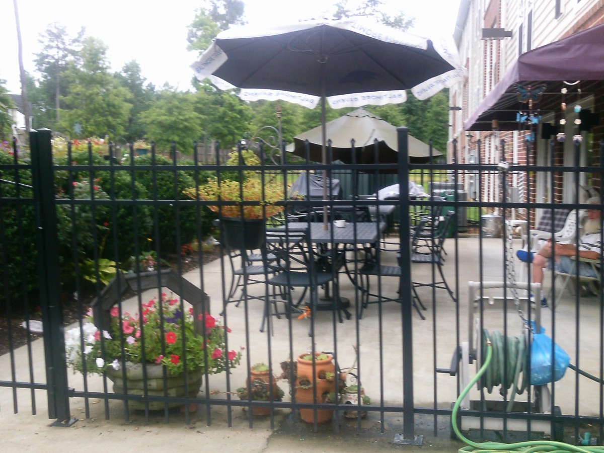 A cozy outdoor patio area with tables, chairs, and umbrellas surrounded by a fence and greenery.