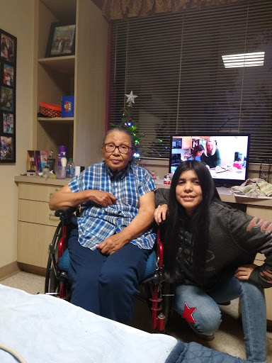 A young woman poses joyfully with an elderly man in a wheelchair, showcasing the bond of family in a hospital setting.
