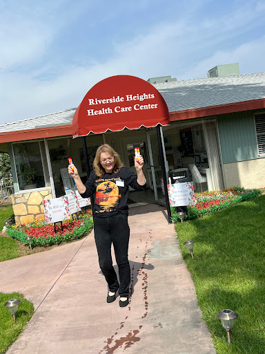 A cheerful individual poses in front of the Riverside Heights Health Care Center, enjoying a sunny day.
