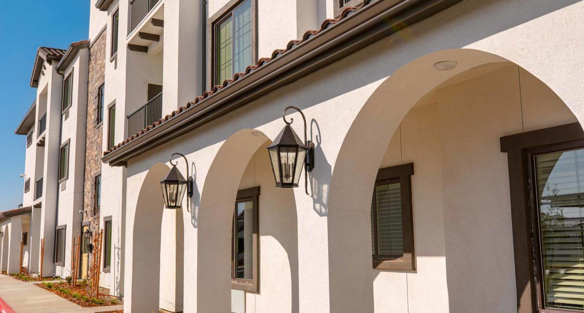 A Mediterranean-style building with arched doorways and decorative lanterns in the sunlight.