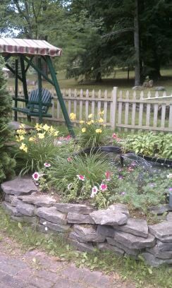 A beautiful garden with colorful flowers and a green swing next to a wooden fence.