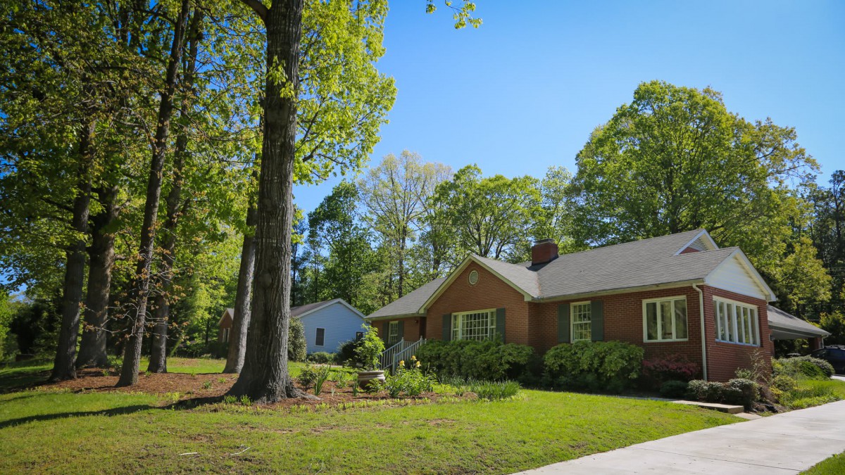 A charming suburban brick house with a lush green lawn and large trees.