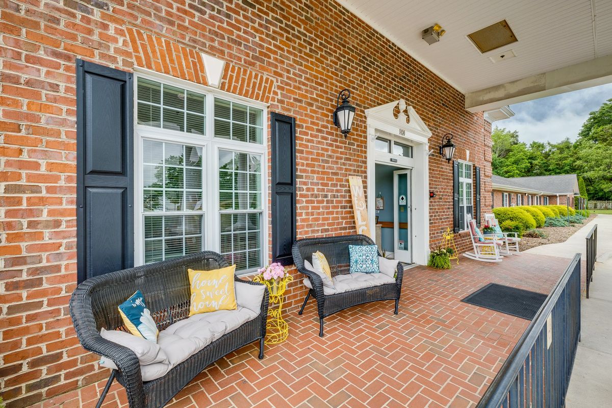 A cozy outdoor patio with seating and decorative cushions against a classic brick wall.
