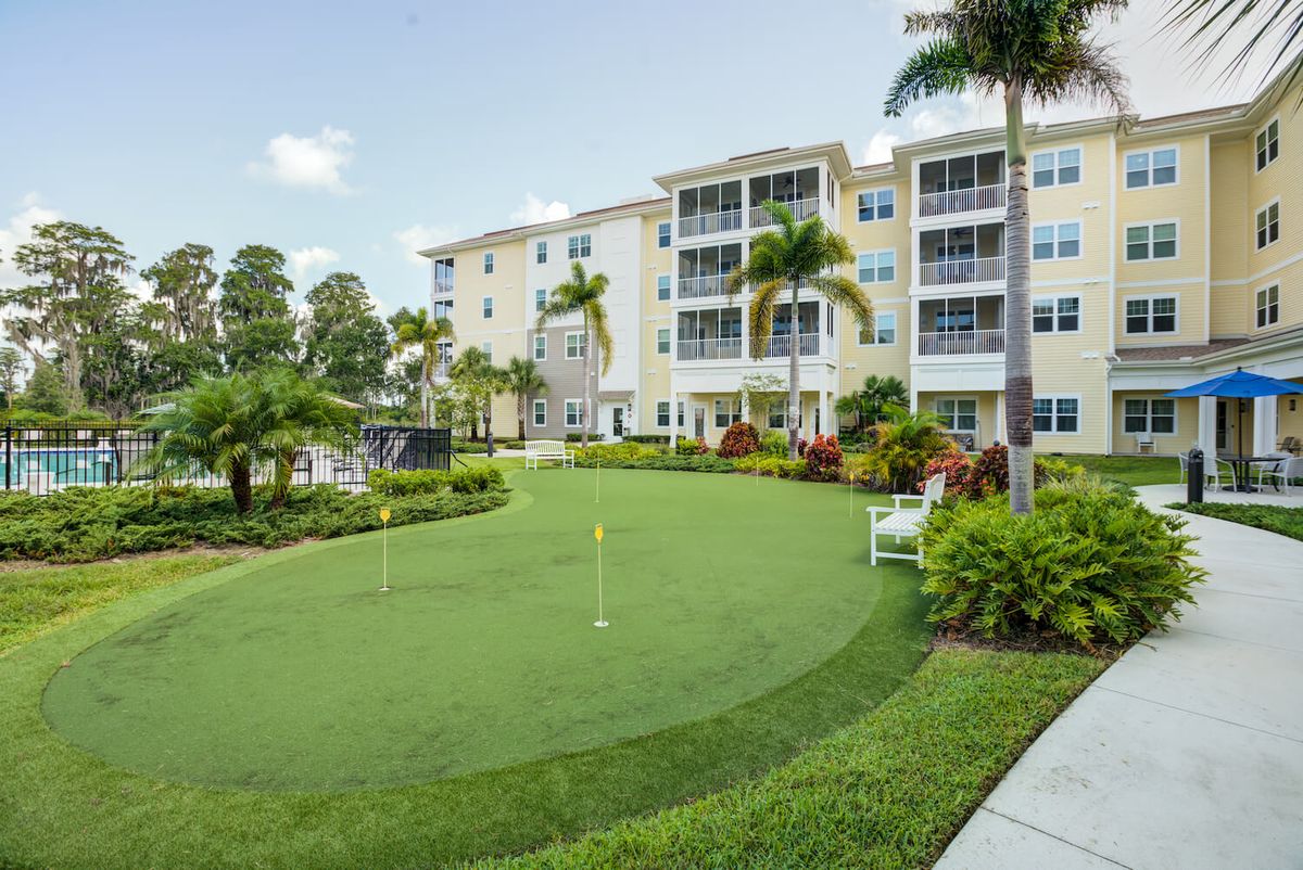 A modern residential building with a landscaped garden and putting green under a clear sky.