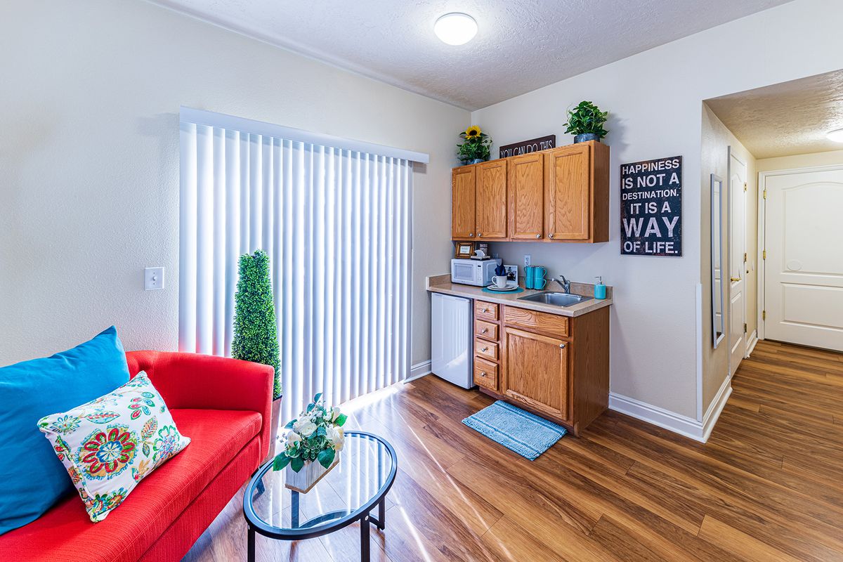 A cozy living area with a kitchenette, featuring a red couch and hardwood flooring.