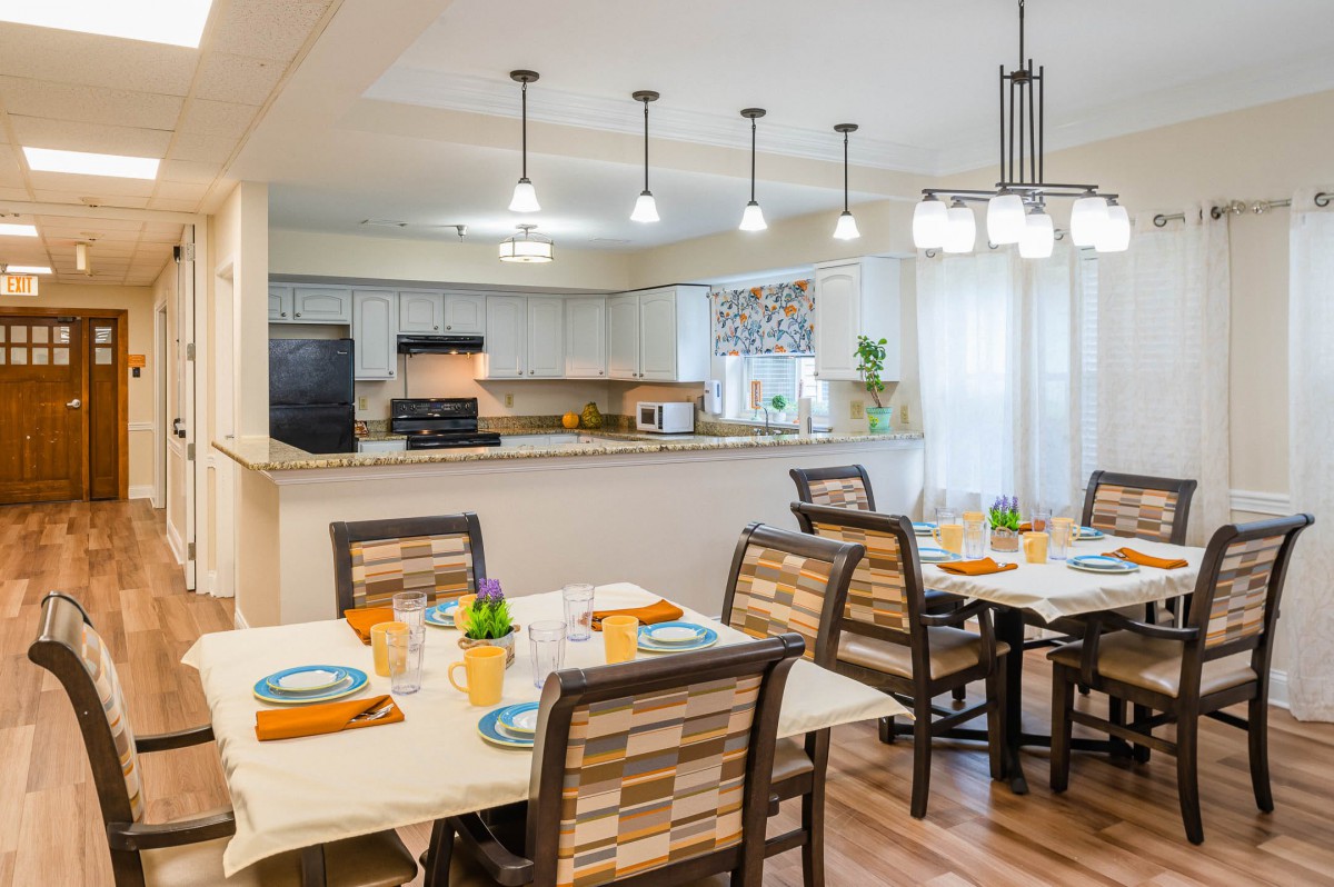 A modern dining area with neatly set tables and a view into the adjacent kitchen.