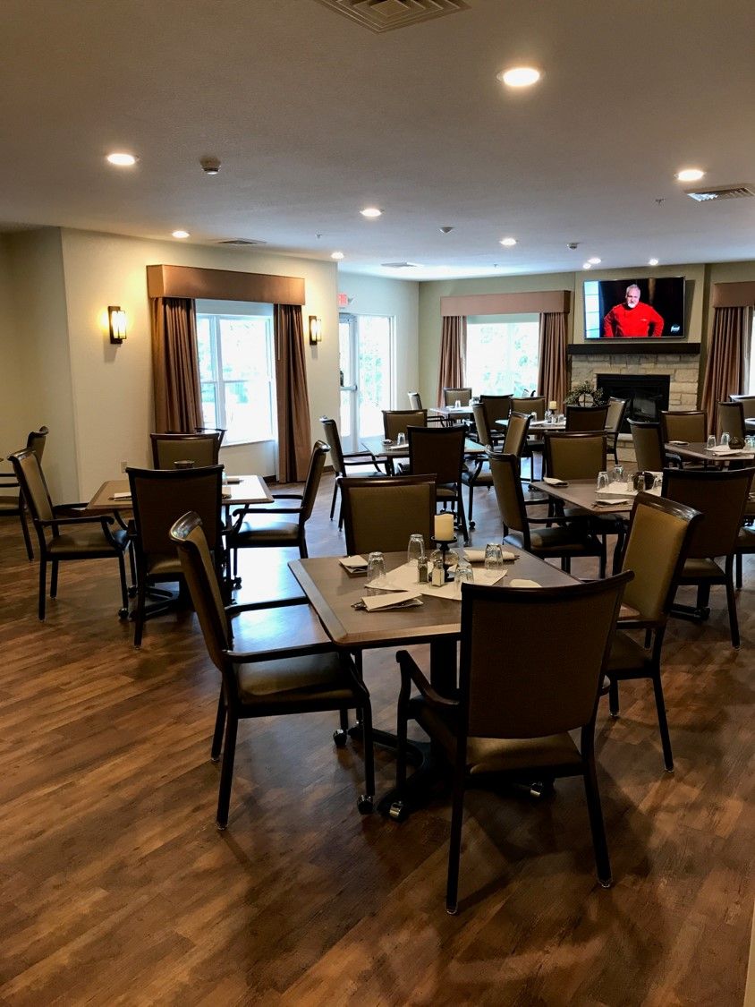 An empty dining room with neatly arranged tables and chairs, featuring a television on the wall.