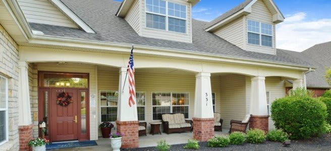 A cozy front porch of a house featuring outdoor seating and an American flag.