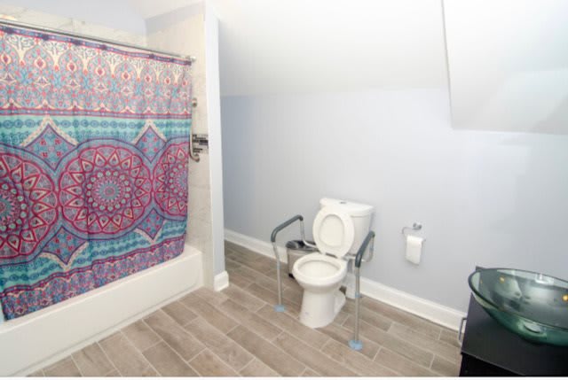 A bathroom with a toilet equipped with handrails, a bathtub, and a colorful shower curtain.
