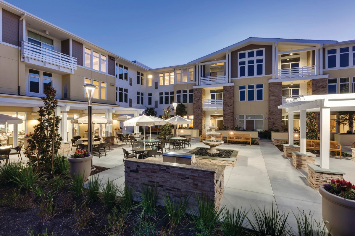 A modern apartment building with a well-lit outdoor courtyard featuring patio seating and landscaping.