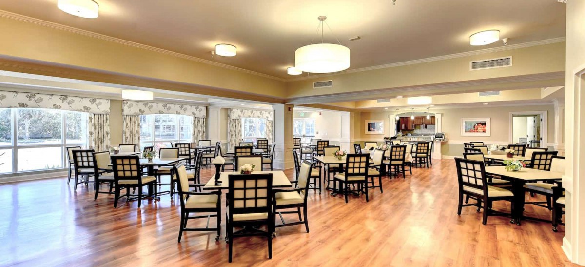 A spacious and elegant dining room with neatly arranged tables and chairs, featuring warm lighting and wooden floors.