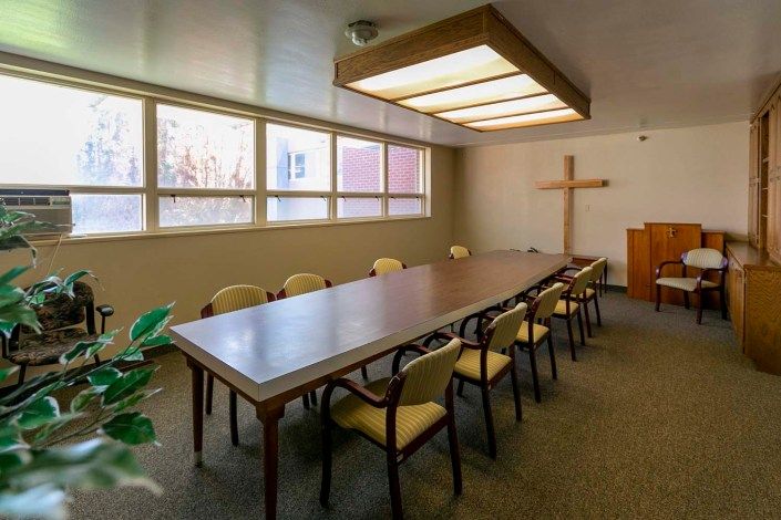 A conference room with a long meeting table, surrounded by chairs, and a cross on the wall.