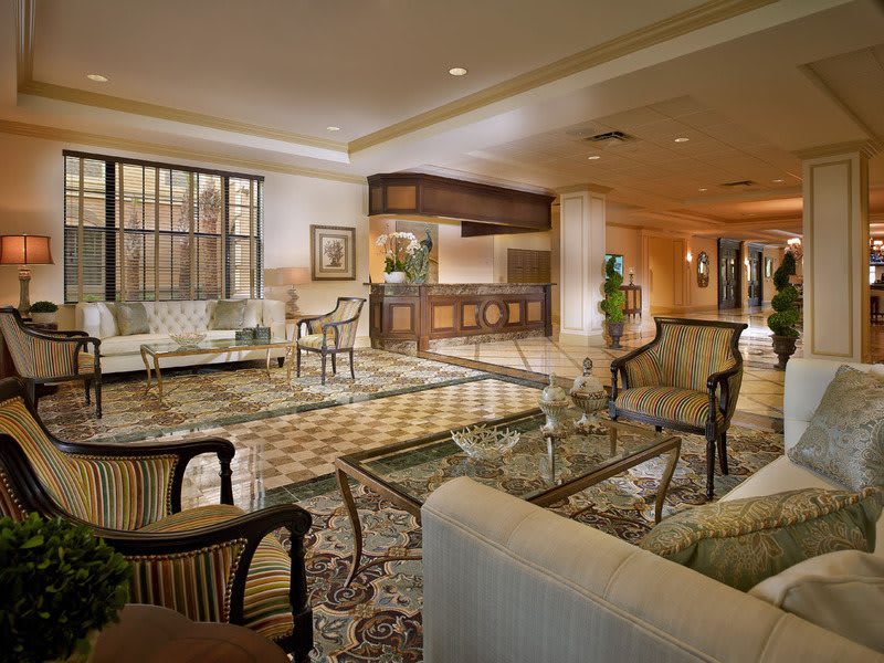 A luxurious hotel lobby featuring a reception desk, comfortable seating areas with armchairs and glass tables, and elegant decor.