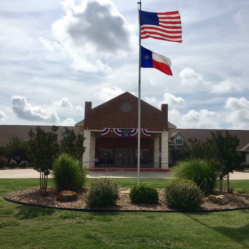 A building with American and Texas flags flying in front, set against a cloudy sky.