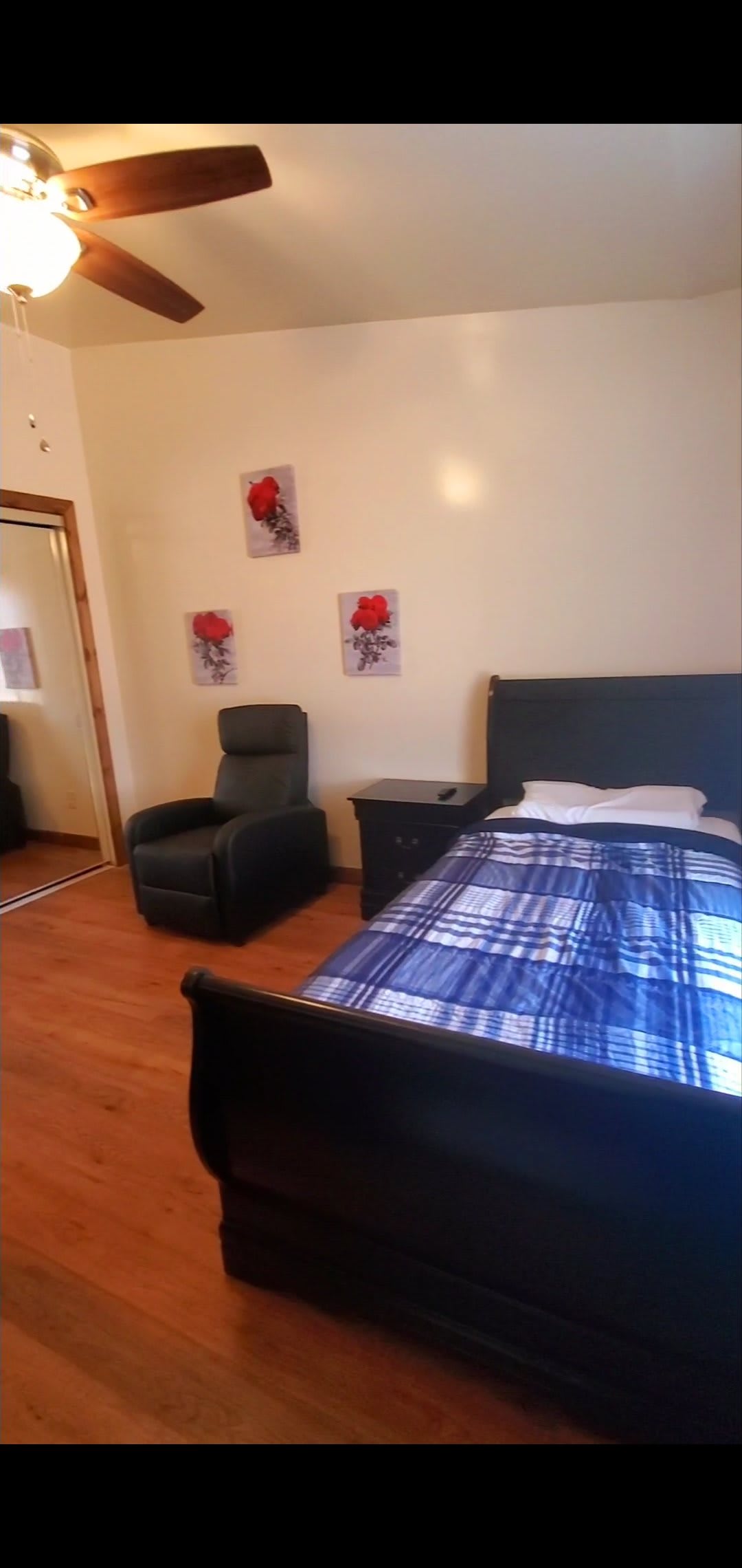 A cozy bedroom featuring a single bed with blue plaid bedding, an armchair, and decorative wall art.
