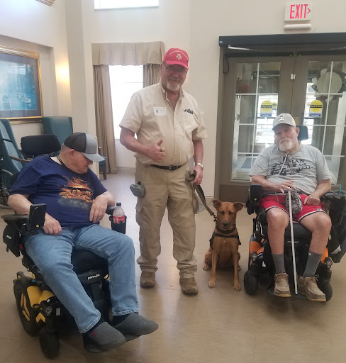 A group of individuals in wheelchairs alongside a service dog, enjoying a moment together indoors.