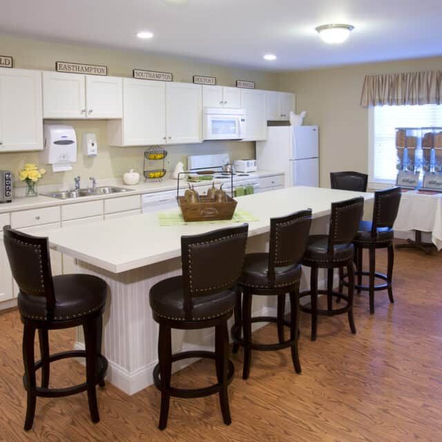 A spacious modern kitchen featuring white cabinets, a large island with bar stools, and wood flooring.