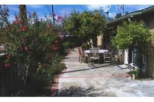 A sunny patio with a table and chairs surrounded by lush greenery and flowers.