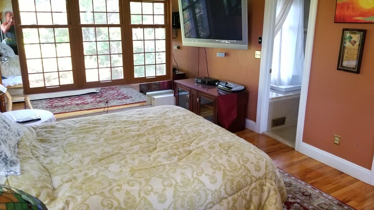 A cozy bedroom featuring a large bed, television, and ample natural light from multiple windows.
