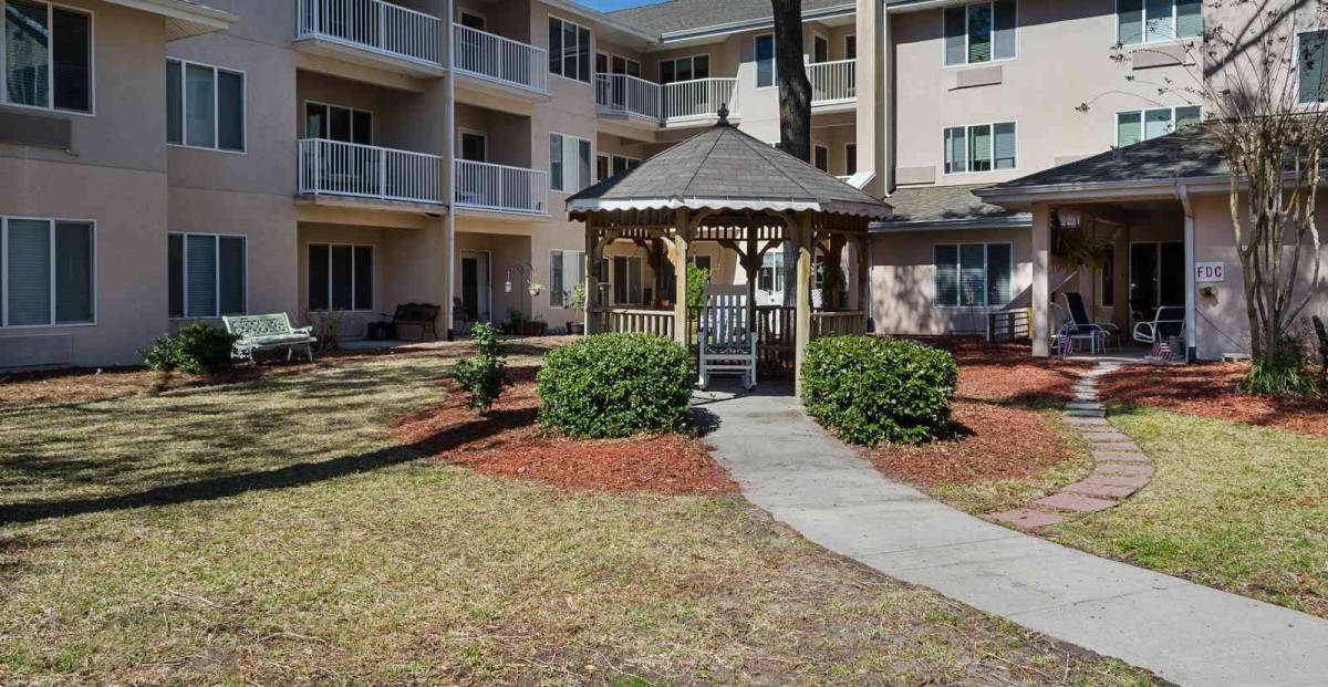 A gazebo situated in the courtyard of an apartment building with a landscaped walkway and bushes.