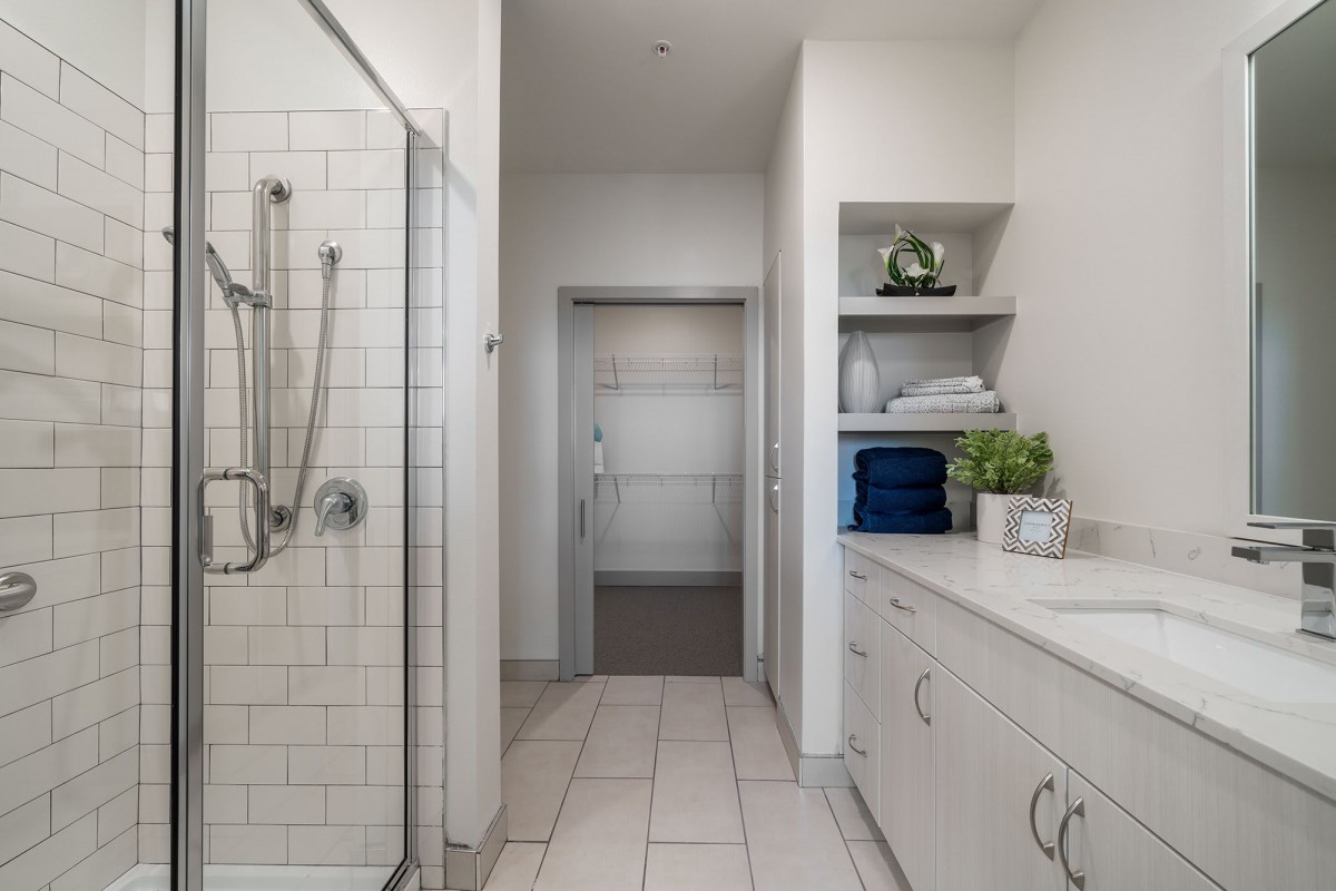 A modern bathroom with a walk-in shower, shelves stocked with towels, and decorative plants.