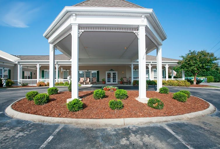 An entrance to a building with columns and landscaped shrubs.