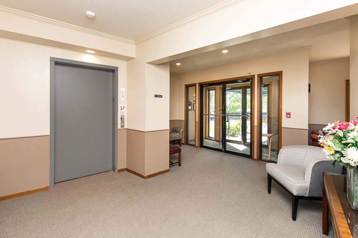 A lobby area featuring an elevator, glass entrance doors, and a seating area.