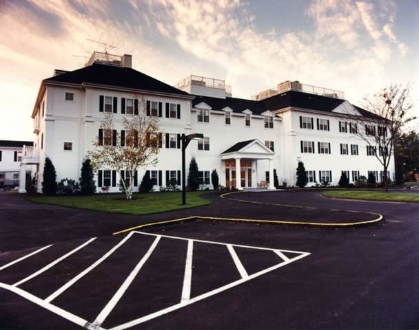 A large white building with multiple windows and a prominent entrance, set against a cloudy sky.