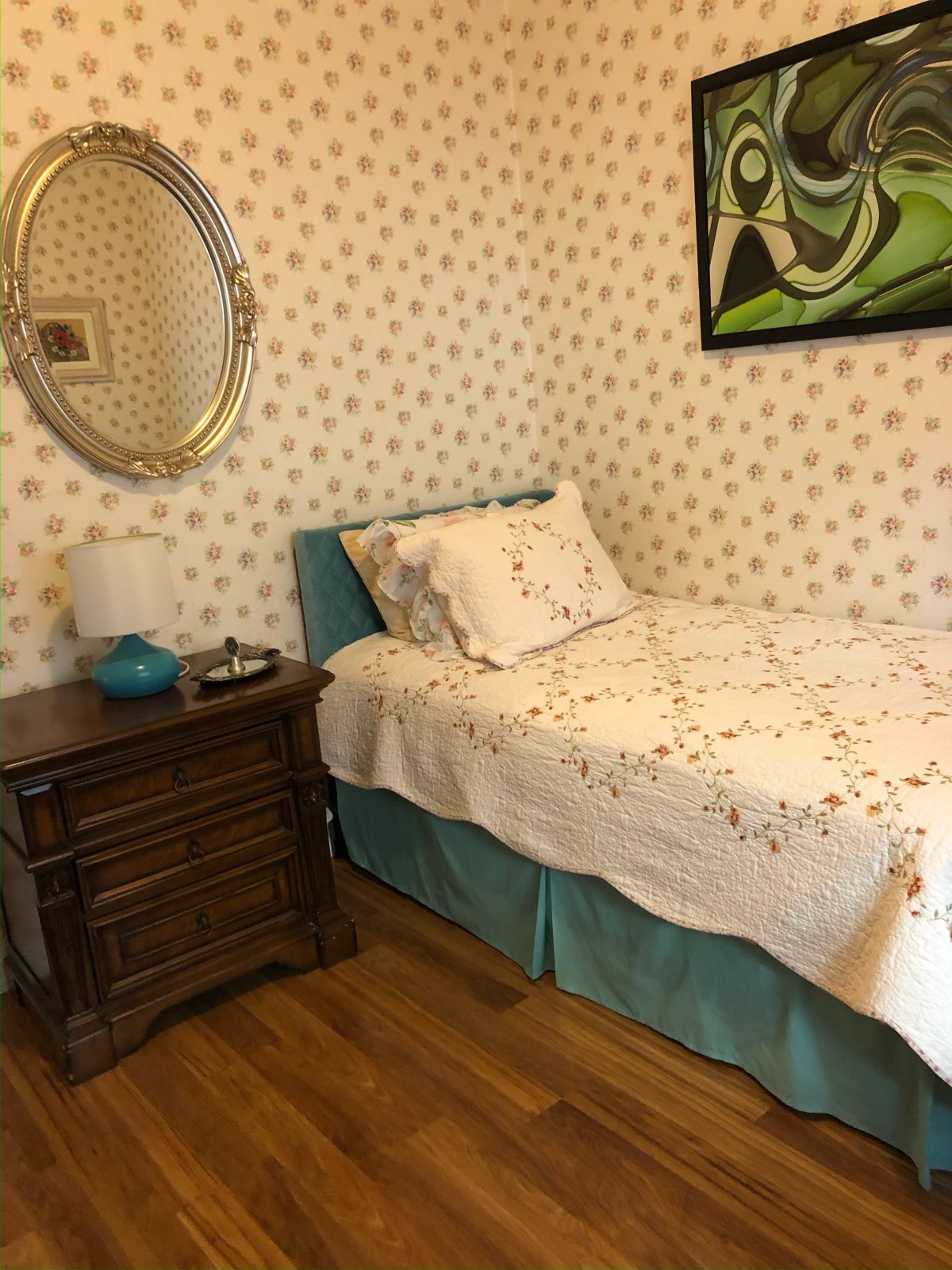 A vintage-styled bedroom with a single bed, ornate nightstand, and floral wallpaper.