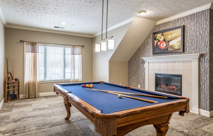 A stylish recreation room featuring a pool table with blue felt, modern pendant lighting, and a cozy fireplace.
