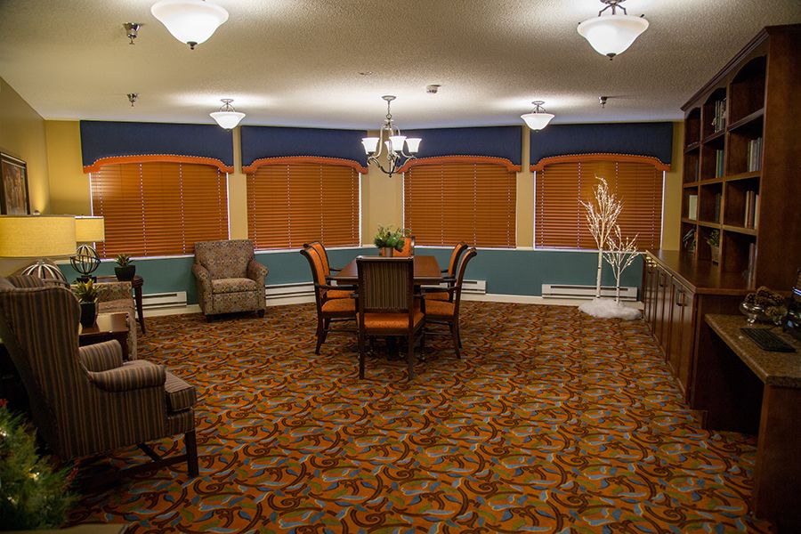 A warmly lit dining area with a central table and chairs, surrounded by armchairs and decorative lighting.