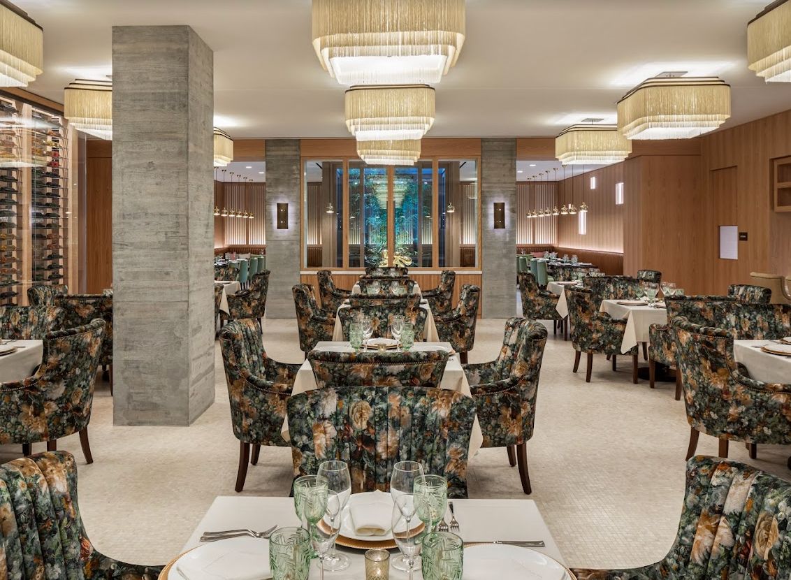 A stylish restaurant interior featuring elegant chandeliers, patterned seating, and neatly set tables.