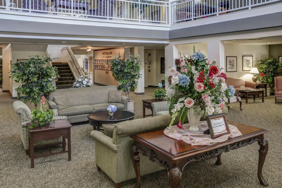 A well-decorated lobby featuring comfortable sofas, a wooden table with flower arrangements, and indoor plants.