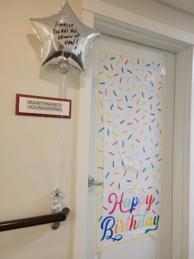 A festive door decorated for a birthday celebration with colorful confetti and a balloon.
