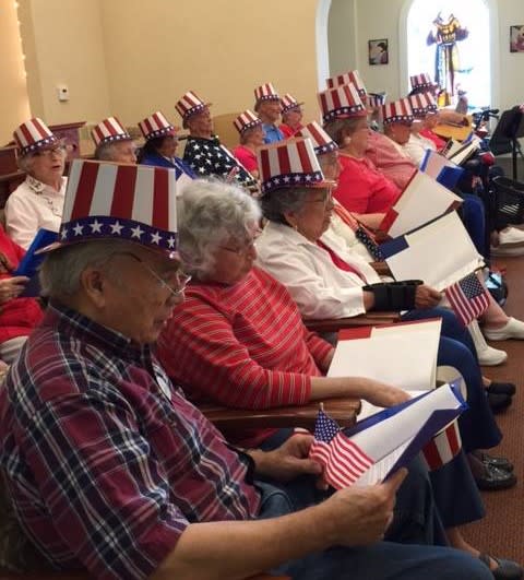 A group of seniors wearing patriotic hats, reading together during a gathering.