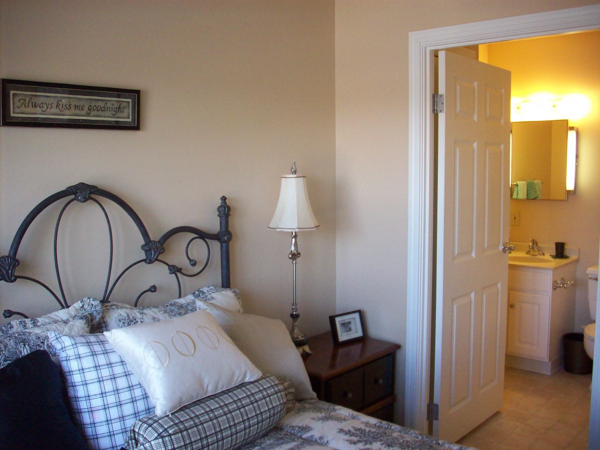 A cozy bedroom with a bed, lamp, and open door leading to another room.