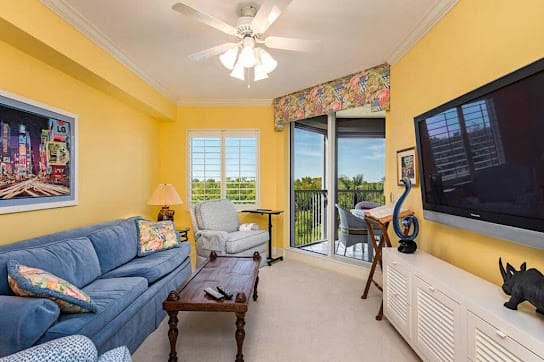 A cozy living room with yellow walls, a blue sofa, and a balcony view.