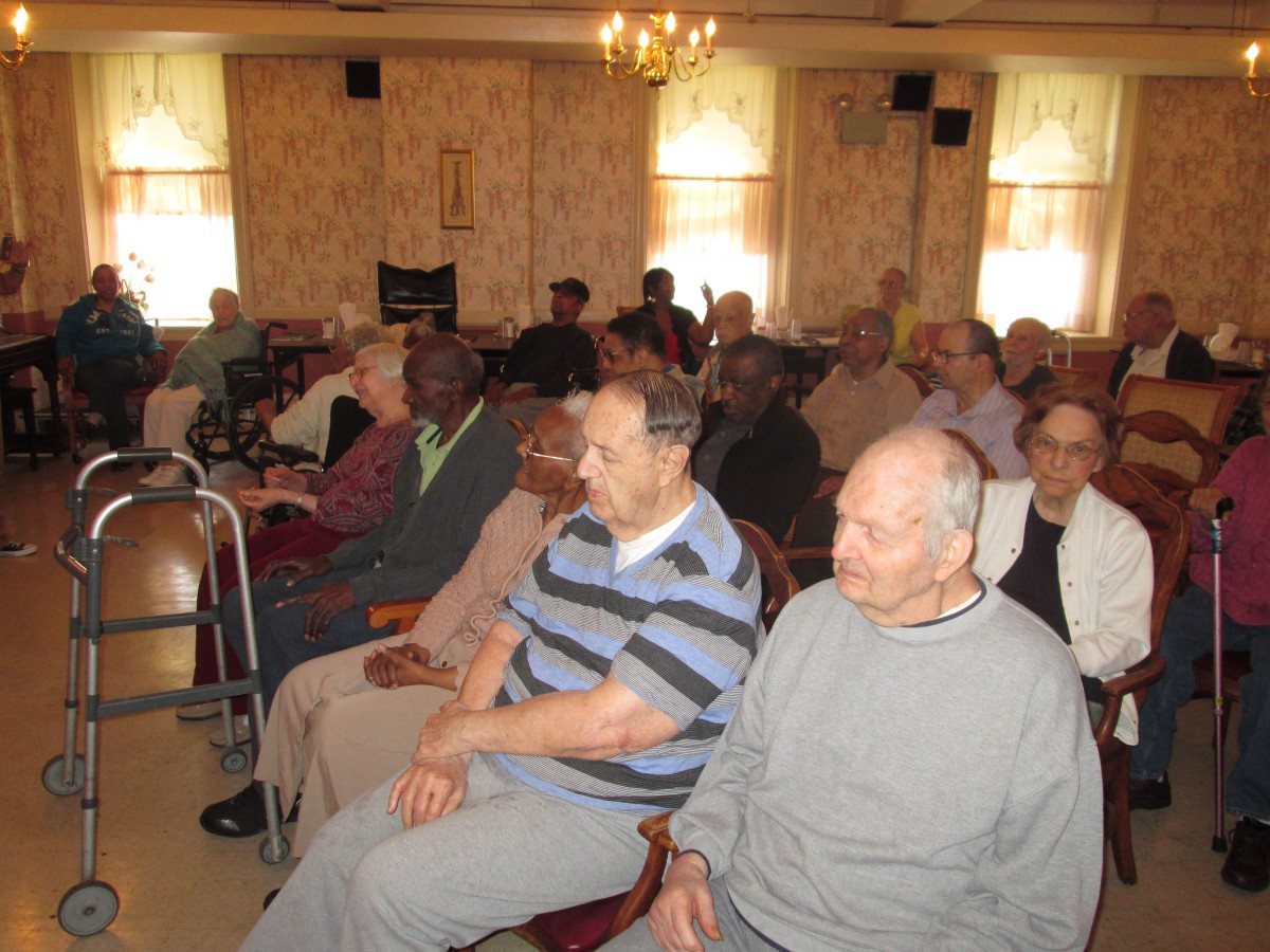 A group of elderly individuals seated in a room, attending an event.