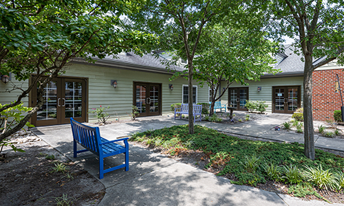 A serene courtyard featuring a blue bench, surrounded by trees and patio area.