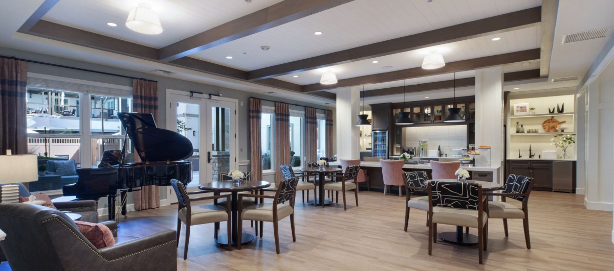 A modern restaurant interior with neatly arranged tables and chairs, featuring warm lighting and wood flooring.