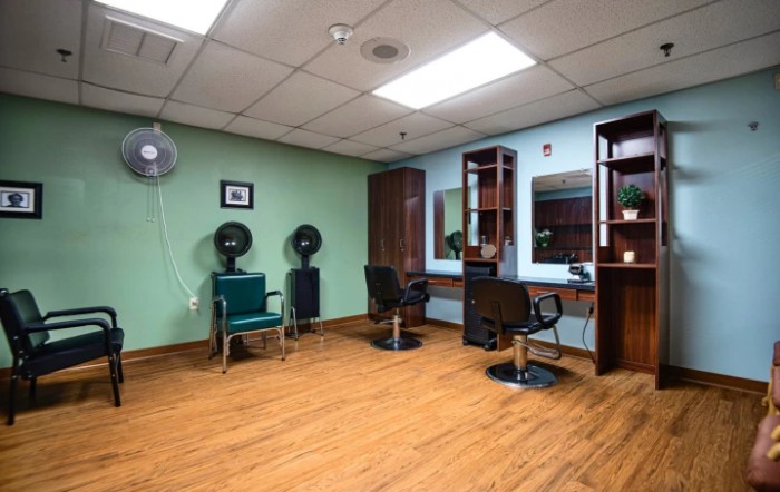 A well-lit hair salon with chairs, mirrors, and hair dryers on a wooden floor.