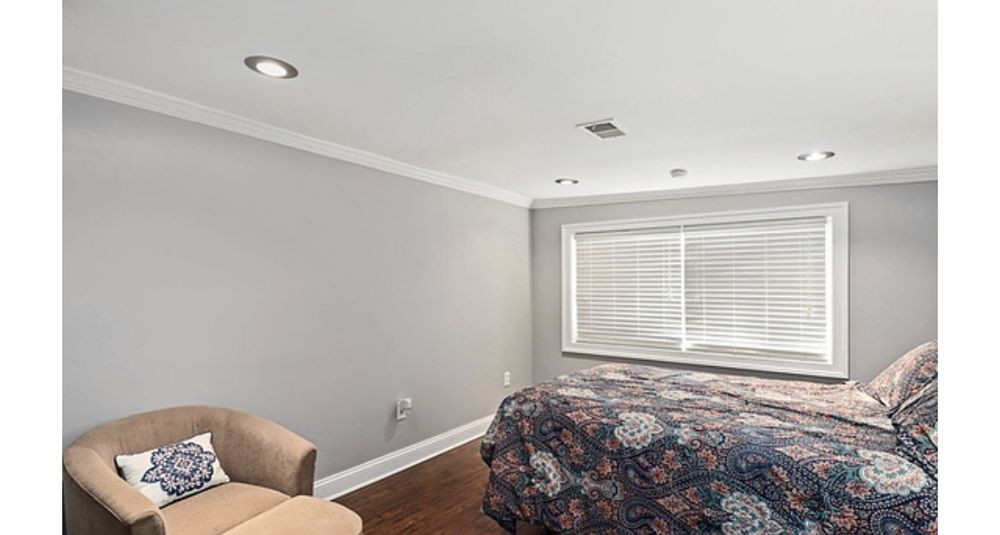 A modern bedroom with minimalist decor featuring a bed, chair, and large window.