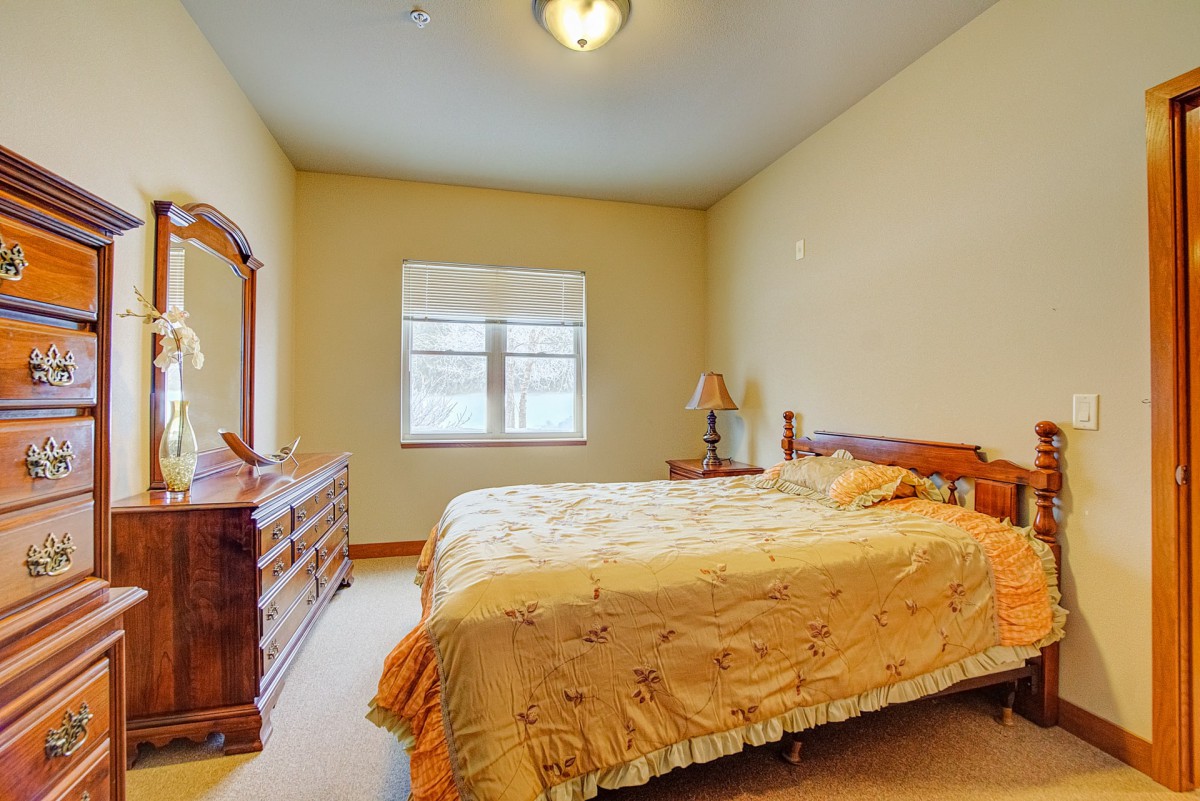 A cozy bedroom with a wooden bed and dresser, lit by natural light from the window.
