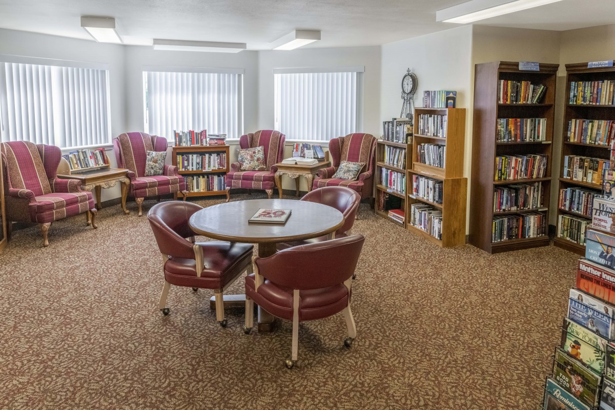 A cozy reading area with bookshelves, chairs, and a table near large windows.