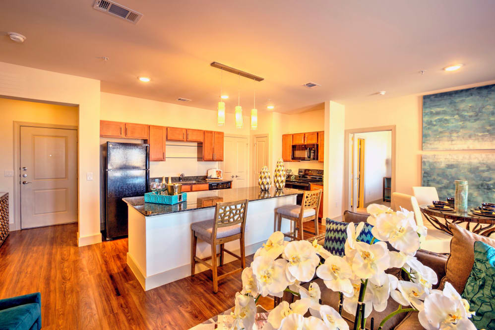 A modern open-concept kitchen with a central island and dining area, featuring warm wood flooring and bright lighting.