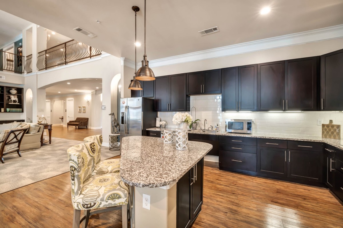 A modern kitchen with a granite island, dark cabinets, and pendant lighting in an open-concept layout.