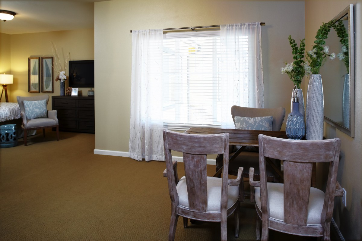 A cozy dining room with a wooden table and chairs near a window covered with white curtains.