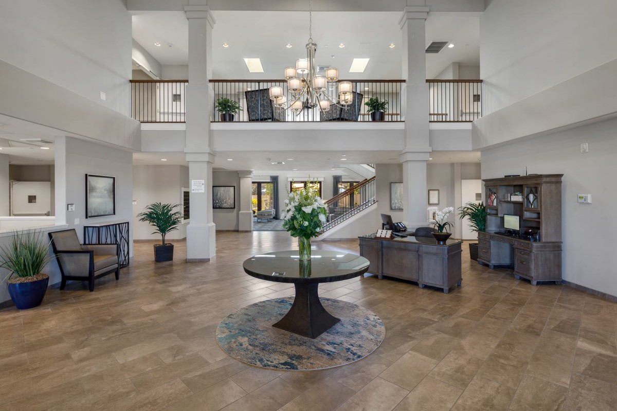 A spacious and elegant lobby with a central table, chandelier, and a staircase leading to an upper floor.