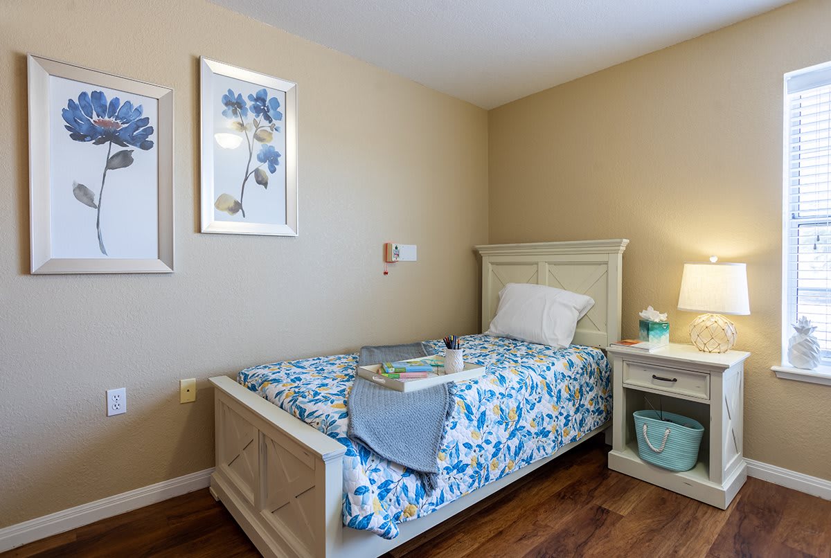 A cozy bedroom with a single bed adorned with floral bedding, complemented by a nightstand and a lamp, creating a warm and inviting atmosphere.